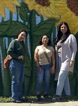 Nancy, Alin, and Zorahila pose in front of sunflower mural